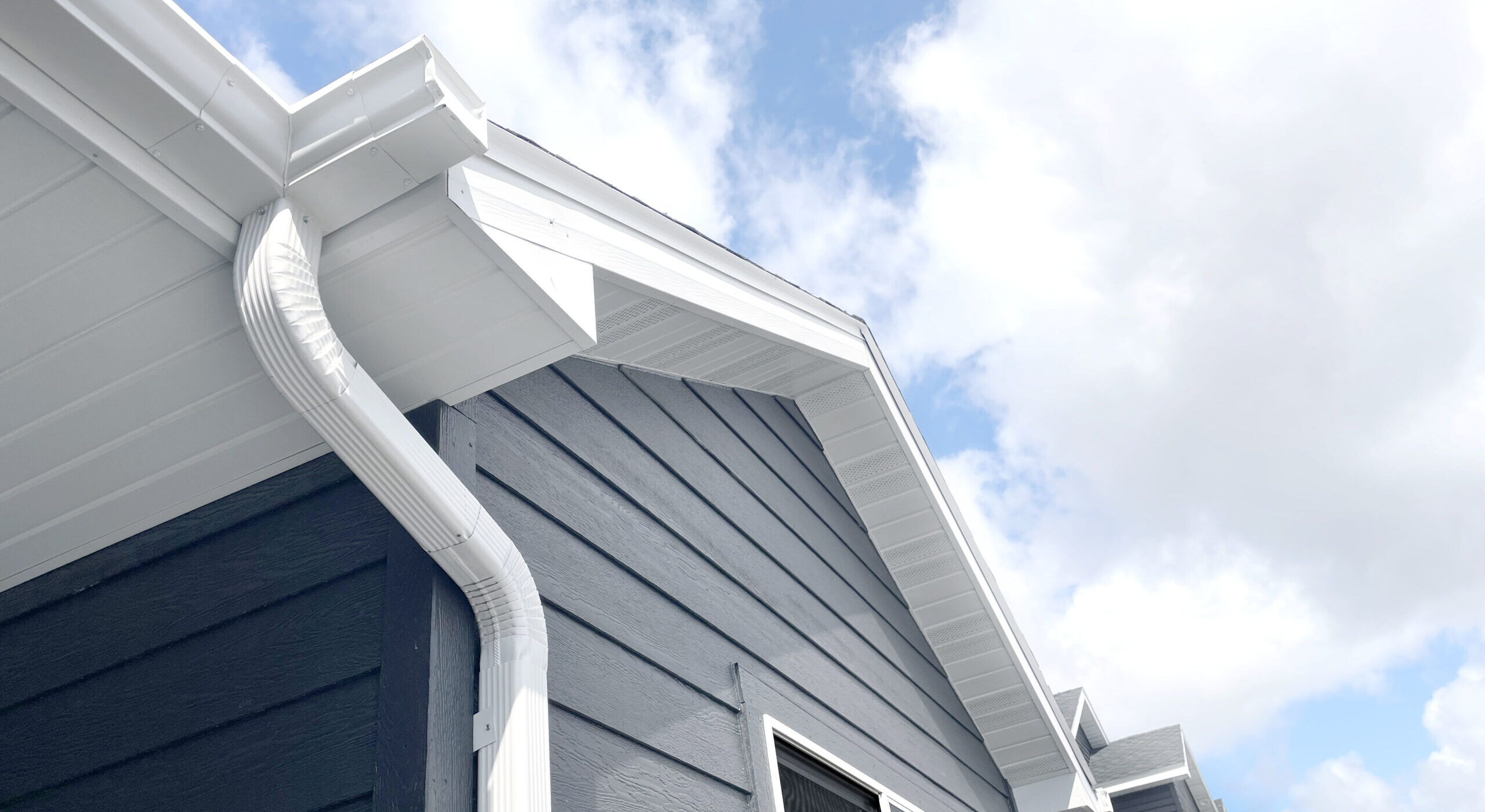 A dark gray home with white gutters and downspouts